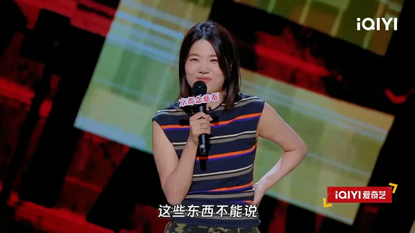 A woman in a sleeveless, striped top, is seen holding a microphone in her right hand.